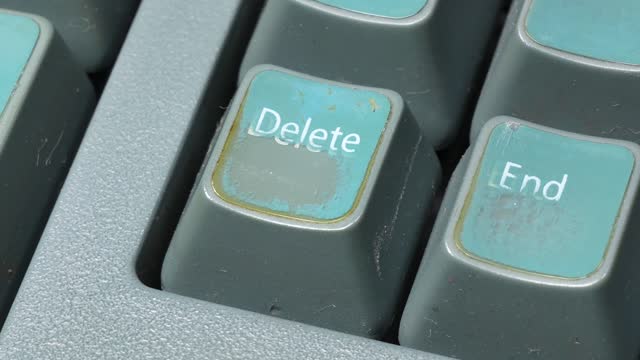 Finger pressing the delete key hard, pushing del button on an old faded worn retro desktop PC keyboard, high angle, detail, macro, extreme closeup Deleting user files, digital data deletion process