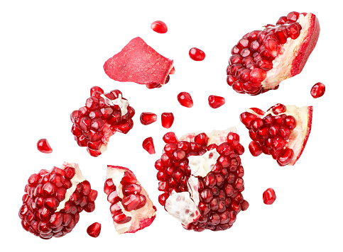 Pomegranate fruit pieces and grains falling close-up on a white background, cut. Isolated