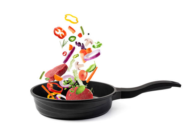 istock Nonstick frying pan with falling beef slices and vegetables on white background. Process of cooking. 1360581279