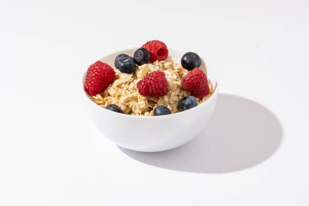 haferflocken mit himbeeren und heidelbeeren in weißer schüssel auf weißem tisch. draufsicht. - oatmeal porridge oat raisin stock-fotos und bilder