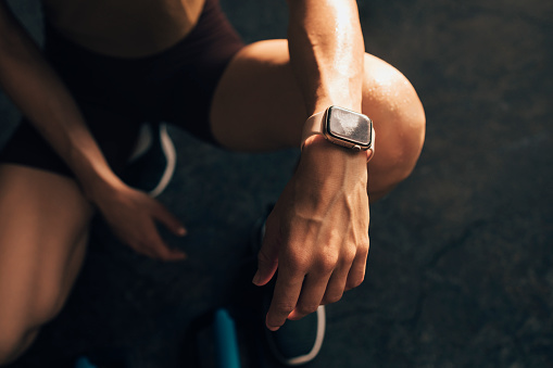 Unrecognizable woman in sportswear looking in her fitness tracker after home workout training.