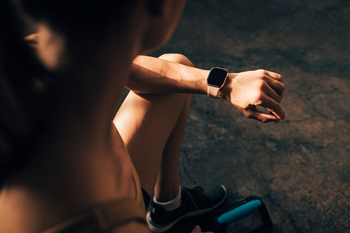 Unrecognizable woman in sportswear looking in her fitness tracker after home workout training.