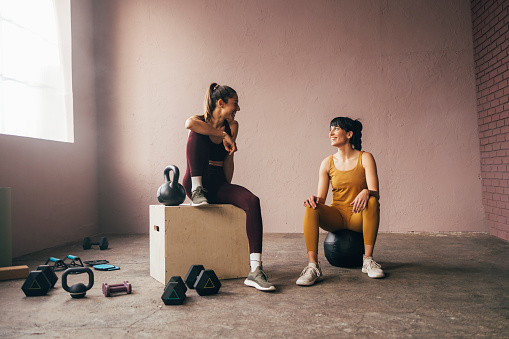 Two smiling woman in sportswear talking while taking a break of workout training.