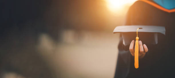 graduates holding black hats with yellow tassels standing with raised diploma in hand over sunset,Concept education congratulation. Graduation Ceremony ,Congratulated the graduates in University. stock photo