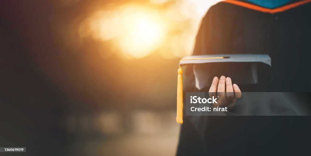 graduates holding black hats with yellow tassels standing with raised diploma in hand over sunset,Concept education congratulation. Graduation Ceremony ,Congratulated the graduates in University. Graduation Stock Photo