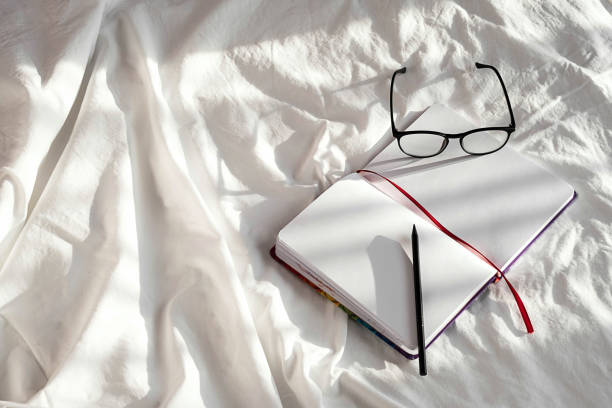 Blank notebook, pencil and eyeglasses rest on white bedding in sunlight with shadows. Stationary still life scene of home office, copy space. Overhead shot, minimal style. Blank notebook, pencil and eyeglasses rest on white bedding in sunlight with shadows. Stationary still life scene of home office, copy space. Overhead shot, minimal style. electronic organizer photos stock pictures, royalty-free photos & images