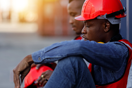 Industrial workers lost their jobs because of the economic downturn. A group of African-American factory engineers or laborers sits saddened by the news of the layoffs.