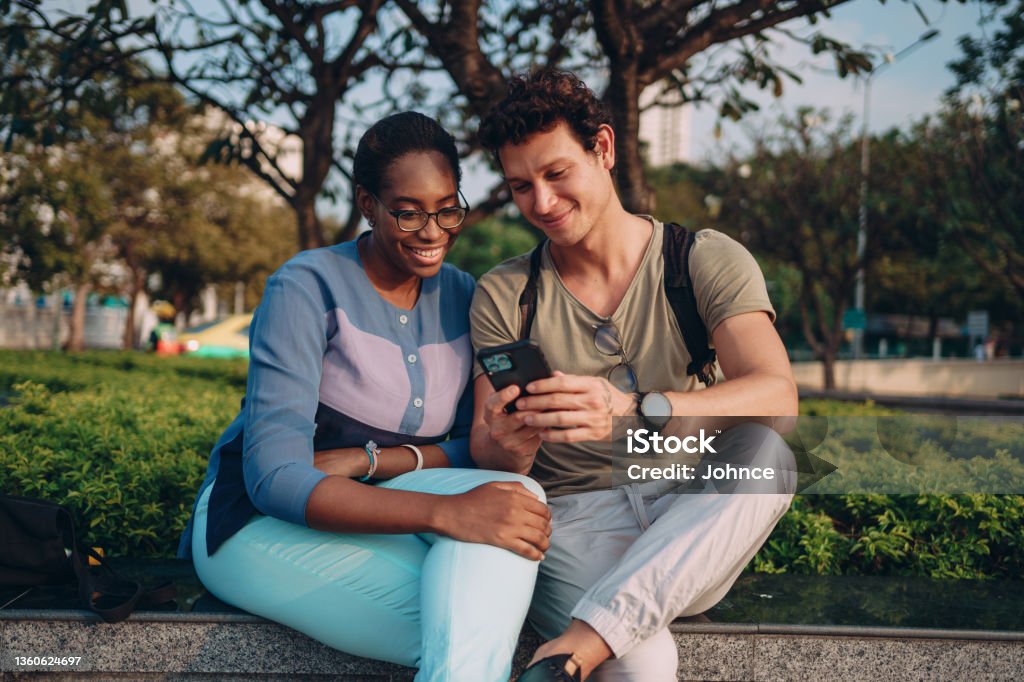 Smiling friends using a phone Smiling couple is sitting outdoor and looking at the phone. Friendship Stock Photo