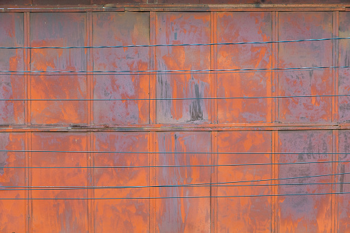 full frame background and texture of rusted steel sheet wall and horiozntal wires in front of it.