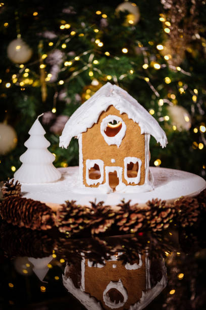 istock Gingerbread house on a table with Christmas tree in blurry background and reflection 1360647770