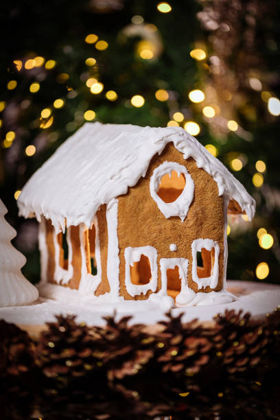 istock Gingerbread house on a table with Christmas tree in blurry background and reflection 1360647776