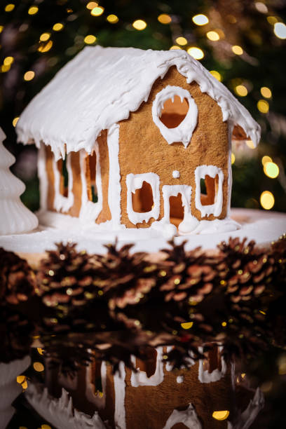 istock Gingerbread house on a table with Christmas tree in blurry background and reflection 1360647778
