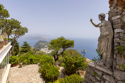 Capri Island; Italy - June 28; 2021: Aerial view from the top of the island Monte Solaro to the Tyrrhenian Sea with rocks Faraglioni; statue of Emperor Augustus in the foreground