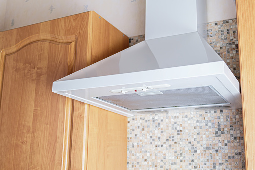 Ceiling metal white cooker hood above the kitchen stove. Modern kitchen appliances. A device for removing the smell of cooking food and tobacco smoke from the air.