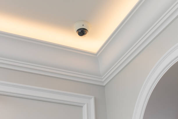 istock Dome surveillance video camera mounted on the ceiling of the classic design room with moldings and ceiling skirting 1360653217