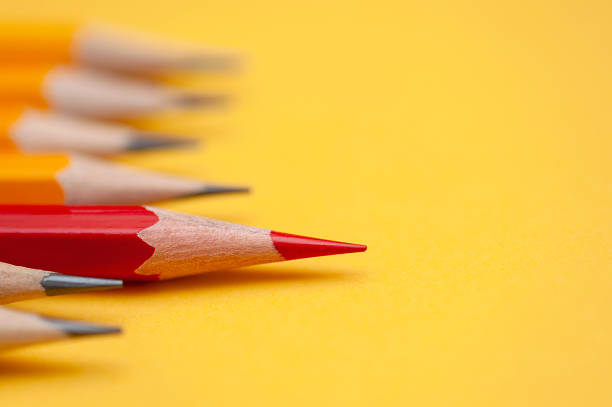 красный карандаш выделяется из группы других карандашей на желтом фоне. - 3683 стоковые фото и изображения