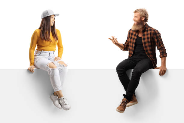 istock Bearded guy sitting on a blank panel and talking to a young casual female 1360656151
