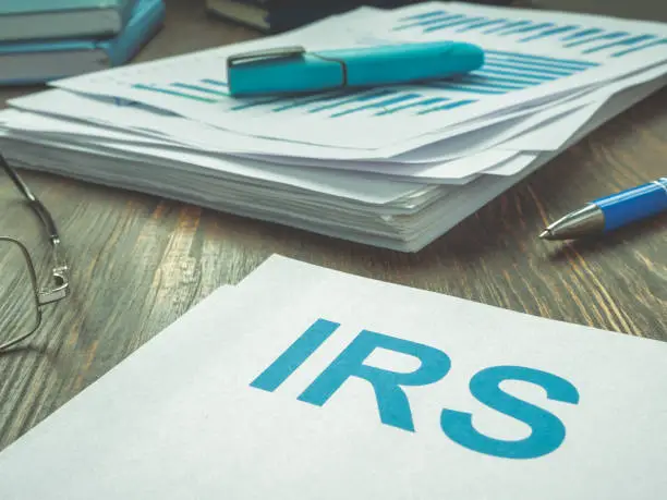 Photo of Abbreviation IRS and stack of financial papers.