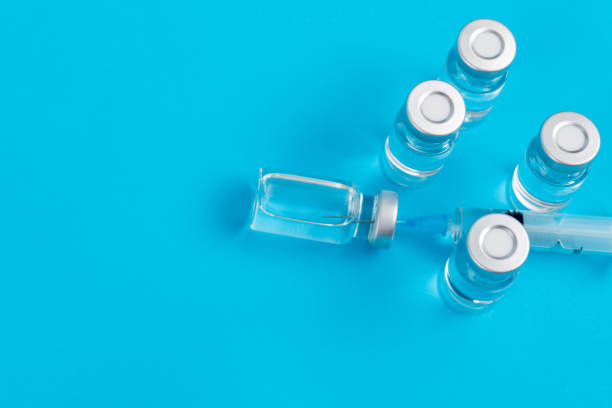 spritze in die durchstechflasche auf blauem hintergrund eingesetzt - syringe vaccination vial insulin stock-fotos und bilder