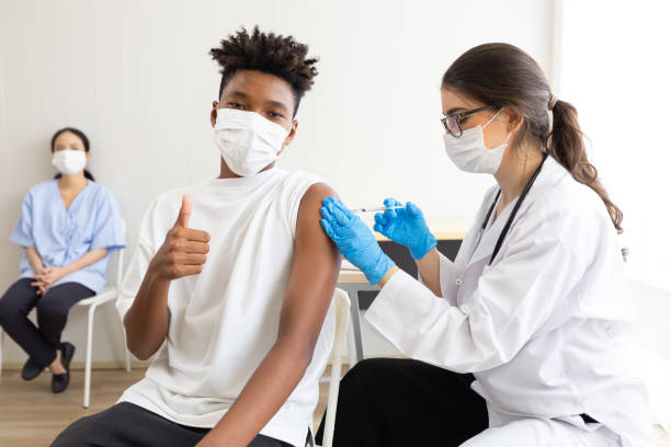 istock young male african wearing medical face mask, thumbs up pose and getting vaccinated from doctor, to build up or maintain immunity 1360665607