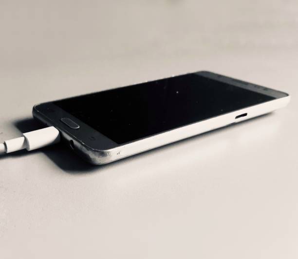 istock Close up of a smartphone on a table connected to a charging cable. 1360665737