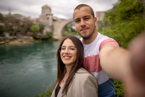 istock Young couple standing near river and making selfie 1360670065