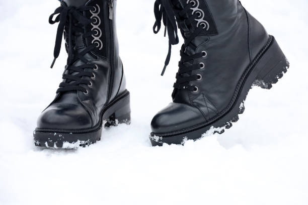 istock Female legs in black leather lace-up boots on a snow 1360670081