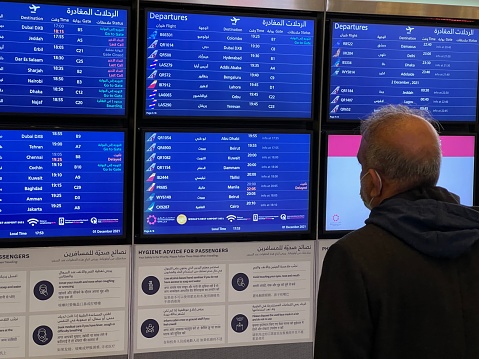 Doha, Qatar - Traveler at Doha international airport looking at the flight information board, checking  flights info. selective focus - December 01, 2021