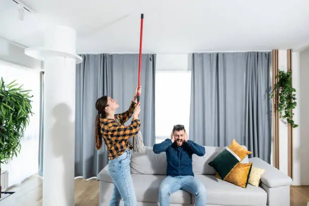 Photo of Young couple stares at the ceiling and yells because a neighbor upstairs is having a party with loud music or renovating an apartment and workers are drilling with heavy tools. Nise pollution concept