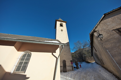 In the Alpes-de-Haute-Provence in Ubaye, late afternoon winter light on the church and the square tower built in 1677 and restored in 1995 in Uvernet-Fours, a village located a few kilometers from Barcelonnette on the road to the Col de la Cayolle in the Bachelard valley