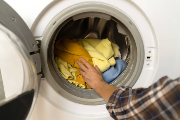 istock Woman puts bright clothes into a washing machine. 1360679827