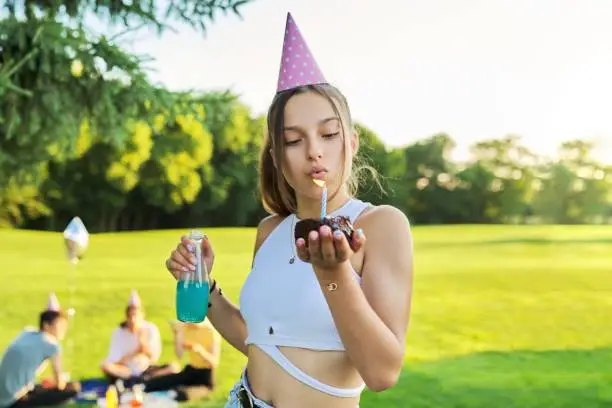 Photo of Birthday, teenage girl in festiv hat with cake blowing out a candle at outdoor party
