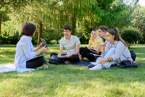 Al aire libre, grupo de estudiantes con maestra sentada en el césped photo