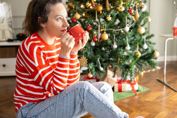 istock Young woman drinking coffee by the Christmas tree 1360681889