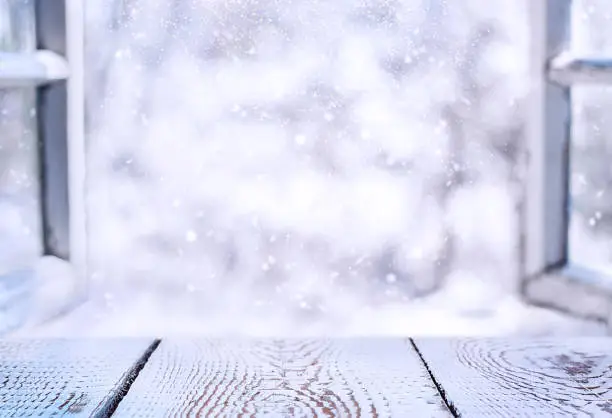 gray wooden surface of the window sill against the background of an open window and a snowy landscape