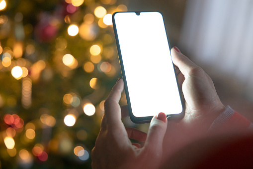 Cropped of woman's hands holding smartphone at Christmas time. Digital mobile phone with copy space area