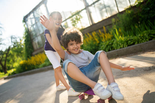 istock Young boy enjoying skateboarding aided by his friend 1360685111