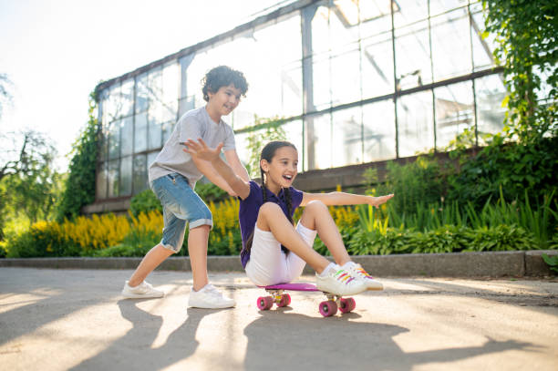 istock Cute kid helping his friend during skateboarding 1360685173