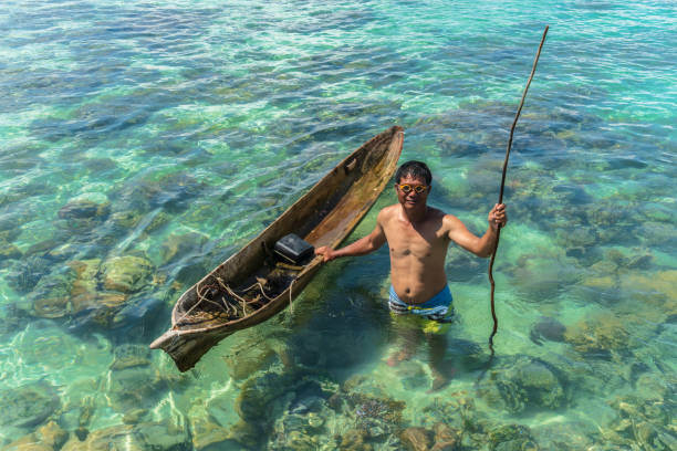 A Bajau Laut fisherman poses with his wooden boat in the turquoise waters of Semporna stock photo