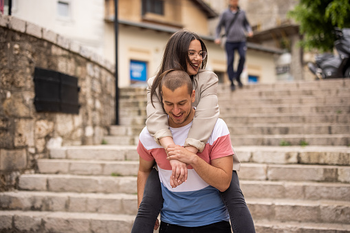 Beautiful smiling young woman enjoying piggyback ride from her boyfriend on staircase