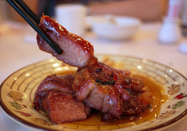 close-up side view chopsticks holding piece of juicy delicious barbecue roasted pork cantonese style close-up side view chopsticks holding piece of juicy delicious barbecue roasted pork cantonese style barbecue pork stock pictures, royalty-free photos & images