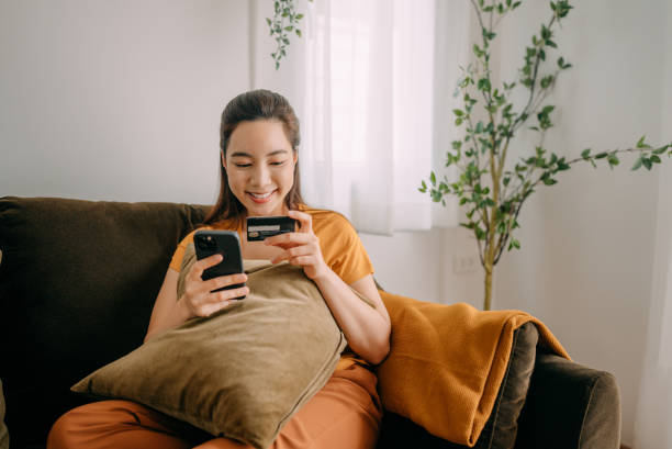 Young woman Using credit card payment Portrait of a smiling asian young woman shopping online on mobile phone using credit card in cafe person paying stock pictures, royalty-free photos & images