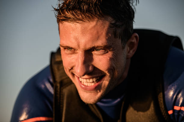 Close-up view of face of cheerful athletic man in wetsuit and vest Close-up view of face of young cheerful athletic man in wetsuit and vest against the background of the sky soaked suit stock pictures, royalty-free photos & images