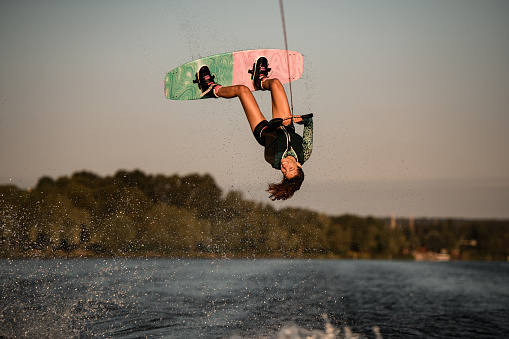 Beautiful view of active female rider holding rope and making extreme jump on wakeboard. Wakeboarding and water sports activity.