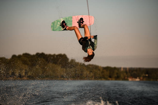 Beautiful view of female rider holding rope and making jump on wakeboard. Water sports activity. Beautiful view of active female rider holding rope and making extreme jump on wakeboard. Wakeboarding and water sports activity. extreme sports stock pictures, royalty-free photos & images