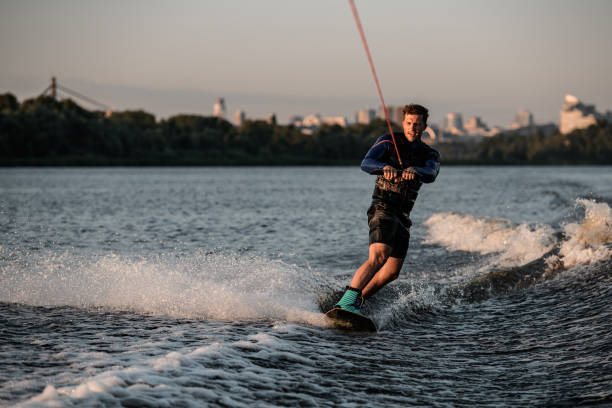 istock Athletic man holds rope and masterfully riding wakeboard on splashing river water. 1360691127