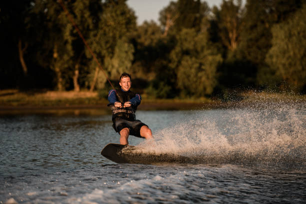 istock Athletic guy holds rope and speedly riding wakeboard on splashing water surface. Active and extreme sports 1360691380