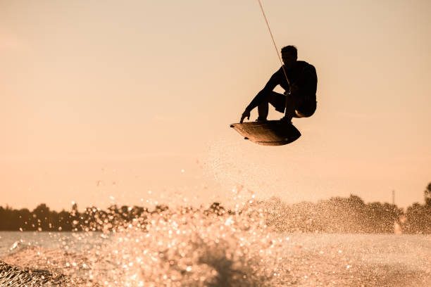ロープを持ち、水�をはね上がってウェイクボードに極端なジャンプをする男性ライダーの美しいシルエット。 - wakeboarding waterskiing water ski sunset ストックフォトと画像