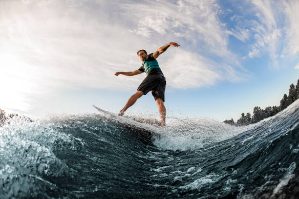 istock young man energetically balancing on wave on wakesurf board on splashing wave. 1360693371