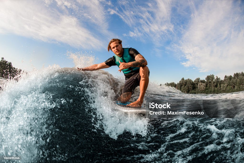 athletic guy wakesurfer skilfully riding down the blue splashing wave on a warm day athletic guy wakesurfer skilfully riding down the blue splashing wave on a warm day. Active water sports Surfing Stock Photo